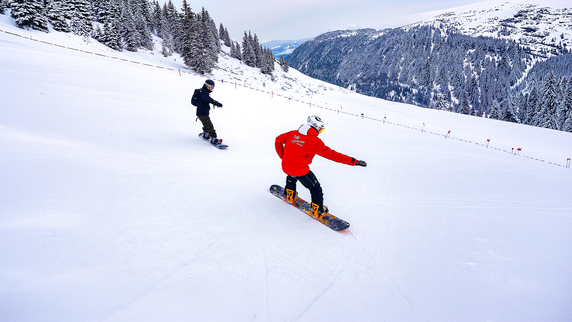 Snowboardlehrer zeigt einem Schüler beim Snowboardkurs in der SkiWelt Brixental die richtige Technik auf der Piste