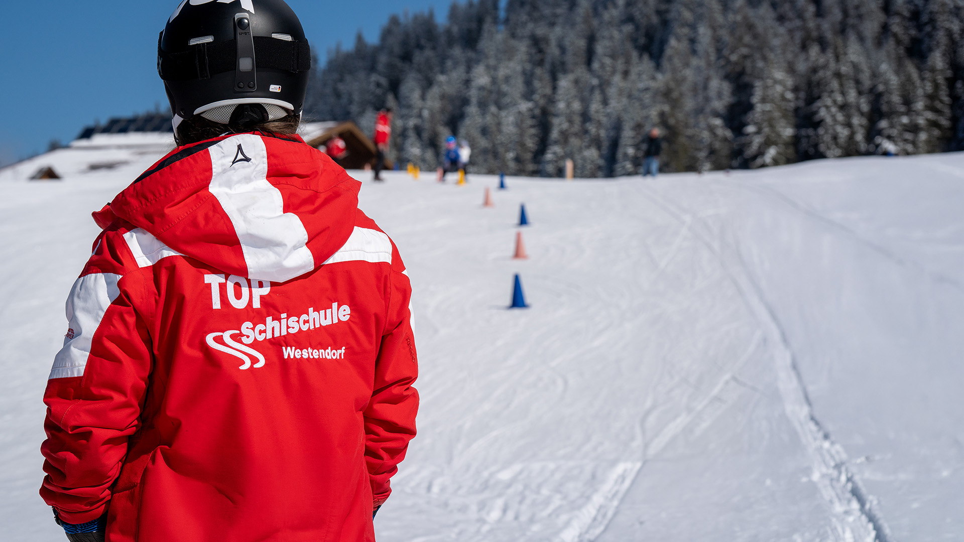 Skilehrer beobachtet die jüngsten Teilnehmer bei einer Abfahrtsübung auf der Piste in Westendorf